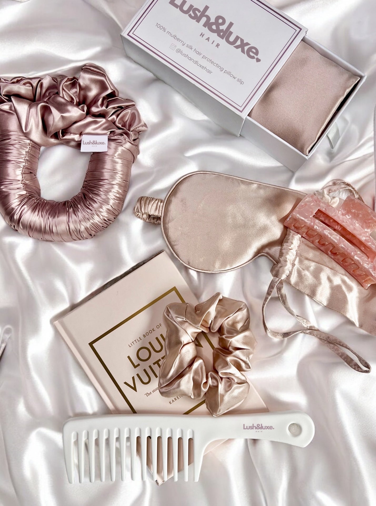 Lush and Luxe Hair product collection flat lay of sleep scrunchie, pillow slip, eye mask, comb, hair claw, scrunchie with a silk background